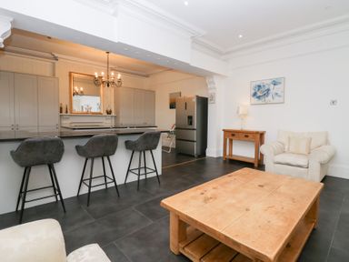 An open plan kitchen and sitting area with bar stools a wooden coffee table armchair and refrigerator at Valley View in Dalton-In-Furness
