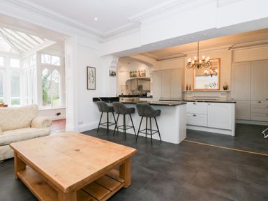 A kitchen with a breakfast bar and three stools a wooden coffee table and a sofa near a conservatory at Valley View in Dalton In Furness