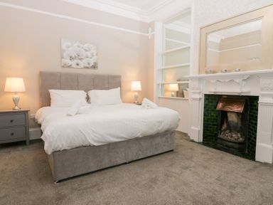 A bedroom with a double bed with white bedding two bedside tables with lamps and a fireplace at Valley View in Dalton-In-Furness