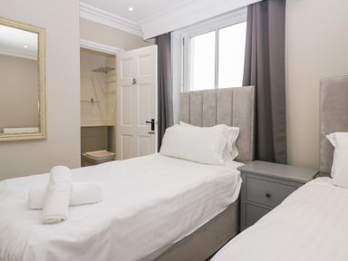 A bedroom with two single beds towels on one bed a bedside table and an open door to a bathroom at Valley View in Dalton-In-Furness