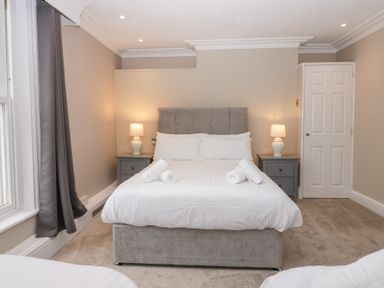 A bedroom with a double bed with white bedding and rolled towels bedside tables with lamps a window with curtains and a door at Valley View in Dalton-In-Furness