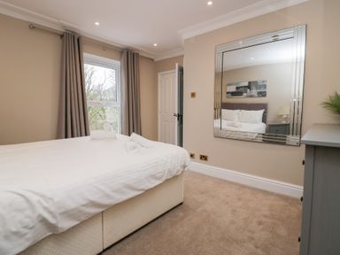 A bedroom with a bed with towels on it a window with curtains a large mirror and a chest of drawers at Valley View in Dalton-In-Furness
