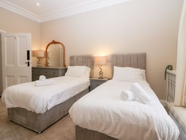 A bedroom with two single beds with rolled towels bedside table with lamp dresser with mirror and lamp at Valley View in Dalton-In-Furness
