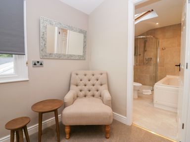 A beige chair with two wooden side tables and a rectangular mirror next to a bathroom with a shower and bathtub at Valley View in Dalton-In-Furness