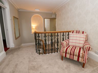 A landing area with a striped armchair next to a decorative railing and a mirror on the wall at Valley View in Dalton-In-Furness