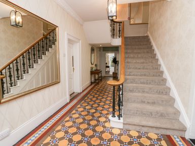 A hallway with patterned tile flooring and carpeted stairs with wooden handrails at Valley View in Dalton-In-Furness