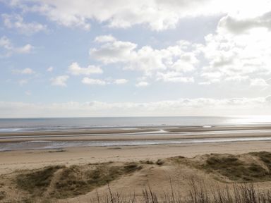 A sandy beach with water channels and sea under a partly cloudy sky at Bridlington Bay House in Bridlington