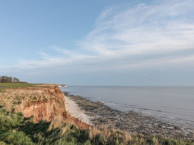 A coastal cliff with grass and rocky shore by the sea under a blue sky at Bridlington Bay House in Bridlington