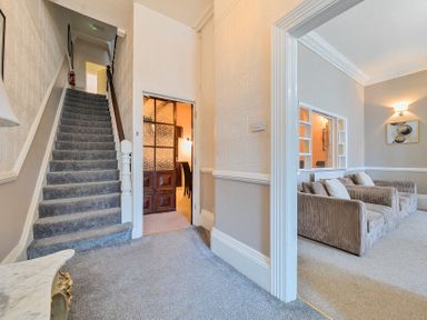 A hallway with a carpeted staircase leading up and a room with two sofas visible at Bridlington Bay House in Bridlington