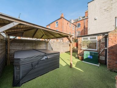 A backyard with a covered hot tub artificial grass and brick buildings at Bridlington Bay House in Bridlington