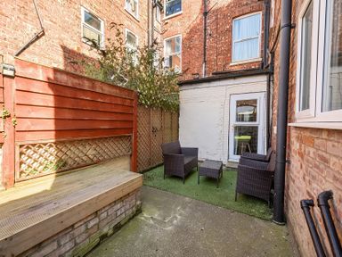 An outdoor patio area with wicker chairs and a table near brick buildings at Bridlington Bay House in Bridlington
