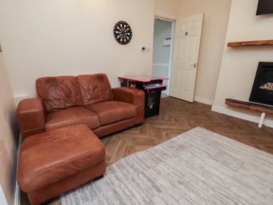 A living room with a sofa, footrest, and a darts board at Bridlington Bay House in Bridlington