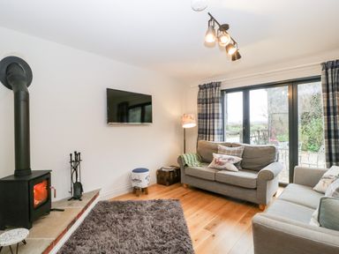 A living room with two sofas a wood burning stove and a wall mounted television at Little Stables Cottage in Spetisbury
