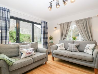 A living room with two gray sofas with patterned cushions and curtains at Little Stables Cottage in Spetisbury