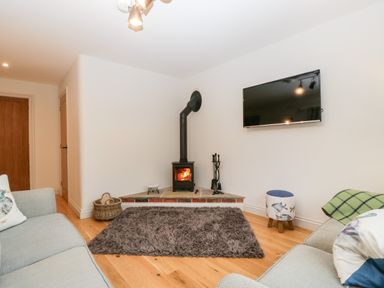 A living room with a wood burning stove a wall mounted TV and two sofas at Little Stables Cottage in Spetisbury
