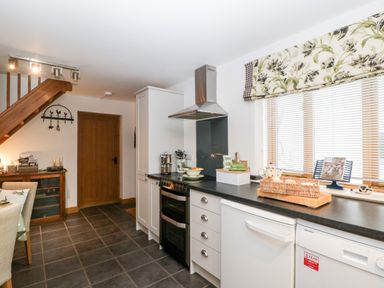 A kitchen with white cabinets a black countertop a stove dishwasher and window with floral valance at Little Stables Cottage in Spetisbury