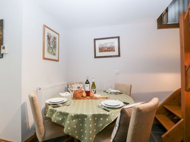 A dining area with a round table covered with a polka dot tablecloth four chairs and framed pictures on the wall at Little Stables Cottage in Spetisbury
