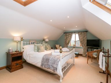 A bedroom with a double bed bedside tables lamps a chair a television and a window with curtains at Little Stables Cottage Spetisbury