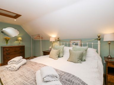 A bedroom with a bed, pillows, bedside tables with lamps, chest of drawers, and towels at Little Stables Cottage in Spetisbury