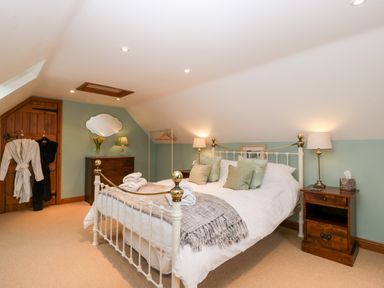 A bedroom with a metal bed frame pillows bedside tables lamps a wooden chest of drawers and robes hanging on a wooden door at Little Stables Cottage in Spetisbury