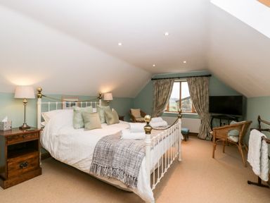 A bedroom with a bed side tables lamps chairs and a television at Little Stables Cottage in Spetisbury