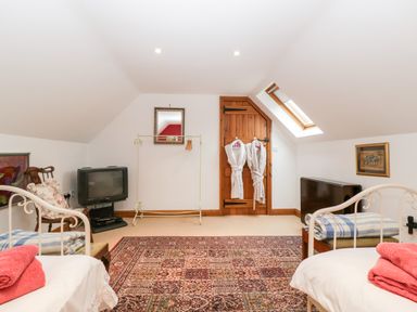 A bedroom with two beds towels on beds a vintage tv a wooden door with robes hanging and a skylight window at Little Stables Cottage in Spetisbury
