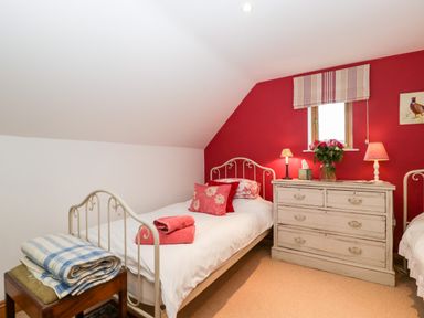 A bedroom with two single beds a chest of drawers and a small window at Little Stables Cottage in Spetisbury