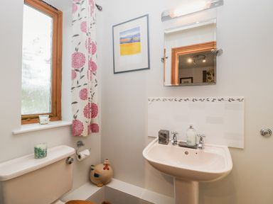 A bathroom with a toilet sink mirror window with floral curtain and decorative rooster at Little Stables Cottage in Spetisbury