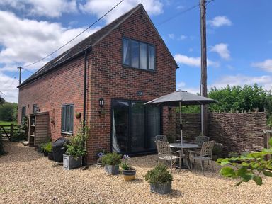 An outdoor area with a brick house a table with umbrella and chairs and several potted plants at Little Stables Cottage in Spetisbury
