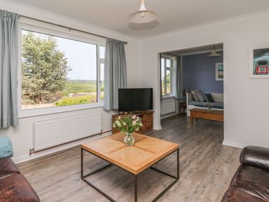 A living room with a wooden coffee table with flowers a television and sofas at Bryn Alaw in Newport Pembrokeshire