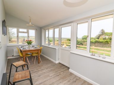 A dining area with a wooden table set for four with yellow chairs and stools by windows overlooking a garden at Bryn Alaw in Newport Pembrokeshire