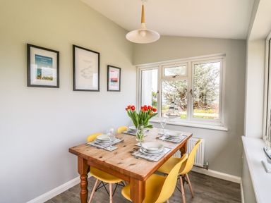 A dining area with a wooden table set for four with yellow chairs and framed pictures on the wall at Bryn Alaw in Newport Pembrokeshire