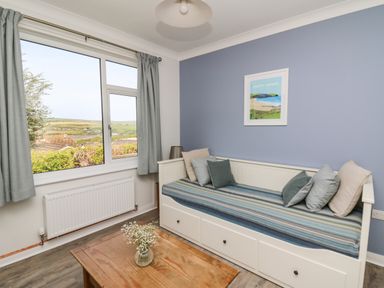A room with a daybed with pillows a wooden table with flowers a window with curtains and a blue wall with framed art at Bryn Alaw Newport Pembrokeshire
