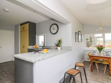 A kitchen with yellow cabinets and breakfast bar next to a dining area with a wooden table and yellow chairs at Bryn Alaw in Newport Pembrokeshire