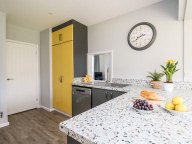 A kitchen with terrazzo countertop yellow cabinets a clock and fruit bowls at Bryn Alaw in Newport Pembrokeshire