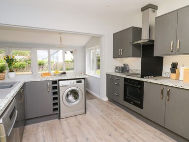 A kitchen with grey cabinets a washing machine an oven and a countertop with bread and fruit at Bryn Alaw Newport Pembrokeshire