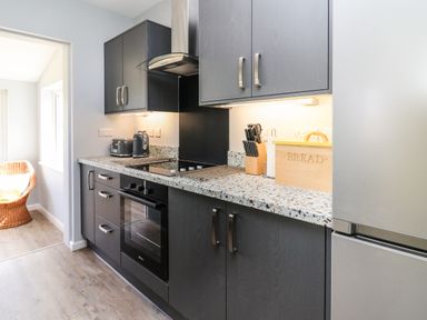 A kitchen with dark cabinets a built in oven a toaster a kettle a wooden bread box and a knife holder at Bryn Alaw in Newport Pembrokeshire