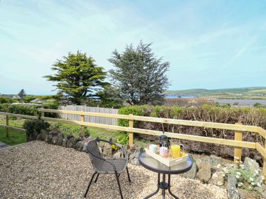 An outdoor patio area with a round glass table and one chair surrounded by a wooden fence and greenery at Bryn Alaw in Newport Pembrokeshire