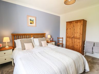 A bedroom with a double bed pillows bedside tables lamps a wooden wardrobe a chair and towels at Bryn Alaw in Newport Pembrokeshire