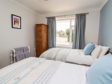 A bedroom with two beds, a wooden wardrobe, grey curtains, a towel rack, and a framed picture on the wall at Bryn Alaw Newport Pembrokeshire
