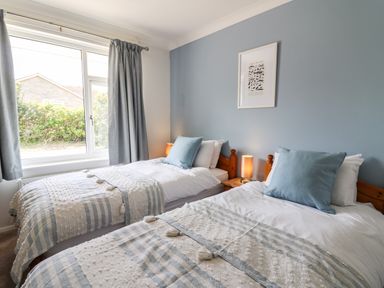 A bedroom with two single beds with blue and white bedding two blue cushions a nightstand with a lamp and a window with blue curtains at Bryn Alaw Newport Pembrokeshire