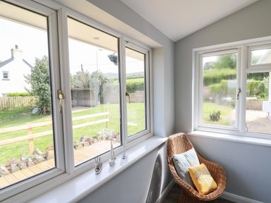 A corner with large windows and a wicker chair with cushions at Bryn Alaw Newport Pembrokeshire