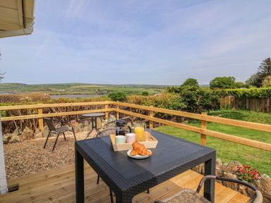 An outdoor patio with a black table and chairs with a tray of drinks and croissants overlooking a green garden and hills at Bryn Alaw in Newport Pembrokeshire