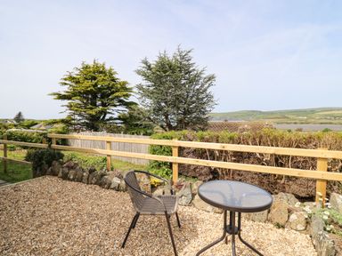 An outdoor patio area with a glass table and a chair overlooking a wooden fence and greenery at Bryn Alaw in Newport Pembrokeshire