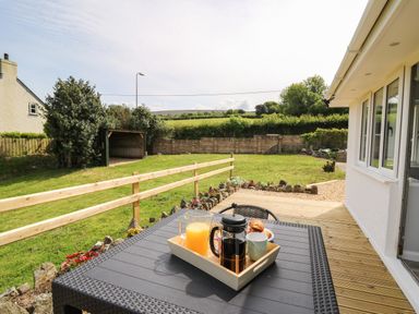 A patio with a table holding a tray of breakfast items and a grassy garden at Bryn Alaw Newport Pembrokeshire