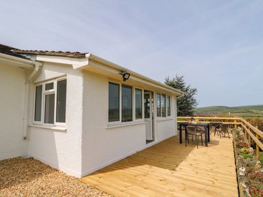 An outdoor wooden deck with a table and chairs next to a white building and a wooden fence at Bryn Alaw in Newport Pembrokeshire