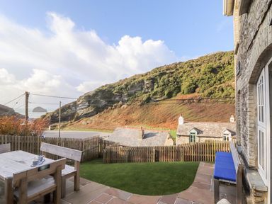 An outdoor seating area with wooden table and benches in a garden overlooking hills and houses at Cliffside in Trebarwith Strand near Tintagel
