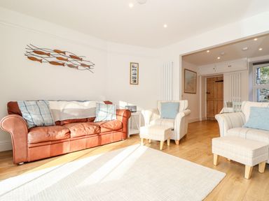A living room with a brown leather sofa and two armchairs with footstools at Cliffside Trebarwith Strand near Tintagel