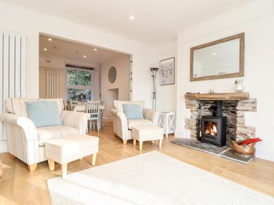 A living room with two armchairs and ottomans next to a fireplace and a dining area in the background at Cliffside in Trebarwith Strand near Tintagel