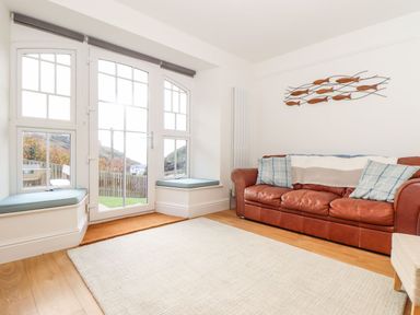 A living room with a leather sofa cushions a rug and window seats by a glass door at Cliffside in Trebarwith Strand near Tintagel